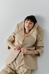 A woman in a beige suit poses against a white wall.