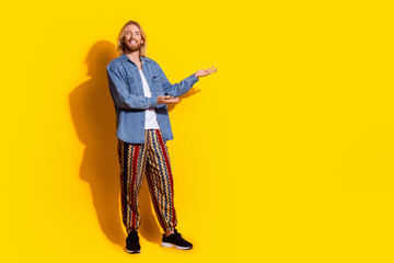 Full body photo of attractive young man point hold empty space dressed stylish denim clothes isolated on yellow color background