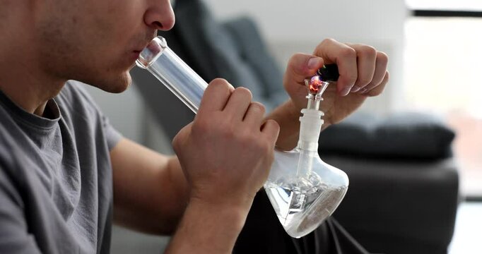 Young male drug addict setting fire to bong and smoking weed closeup 4k movie slow motion. Addiction to marijuana concept