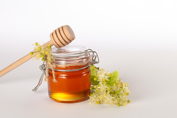 A jar of liquid honey from Linden flowers, stick with honey and fresh flowers on a white background.Copy space.Close up