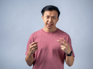 An Asian man in a pink shirt smiles and flashes a peace sign with both hands, exuding a cheerful and relaxed demeanor. The plain light blue background highlights his positive and friendly expression.