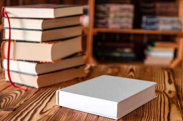 Books. A white notebook with space for text lies on a wooden table against the background of bookshelves
