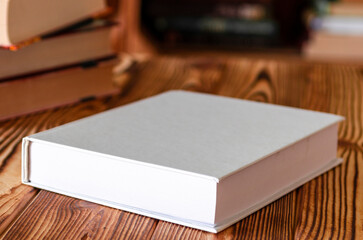 Fototapeta premium Books. A white notebook with space for text lies on a wooden table against the background of bookshelves