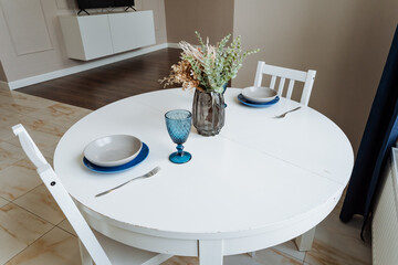The house interior features a charming rectangular wooden table decorated with plates, glasses, and a vase of flowers, adding to the warm and inviting atmosphere of the space