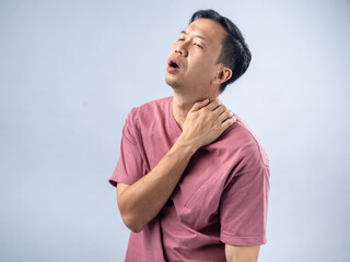 A man in a pink shirt holds his shoulder with a pained expression, indicating shoulder pain or discomfort. The plain light blue background emphasizes his distress