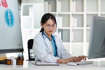 Female Doctor Working on Computer in Modern Medical Office with Medical Equipment and Bookshelves in Background