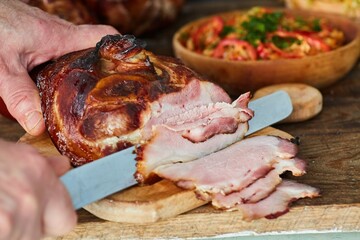 The cook's hands cut a large piece of meat baked in the oven. Meat production