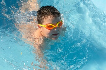 cheerful boy wearing goggles enjoys a playful moment in the pool, embodying the spirit of summer fun