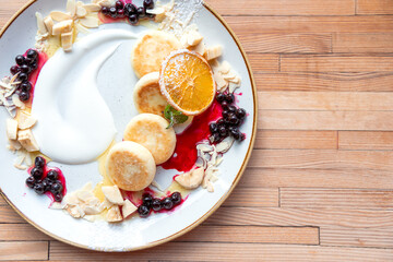 High Angle View Of Food With Cup of Coffee On Plate On Table. Directly above view of freshly home-cooked Syrniki with jam served on a white plate with cup of cappuccino against wooden background close