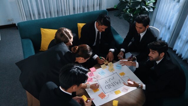 Top view of skilled businesswoman write marketing idea and placed sticky notes on mind mapping while planning financial strategy with diverse business group. Startup team working together. Directorate