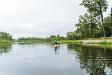 Obraz premium Rafting on the river among the trees on a SUP, SUP boarding, rowing standing, traveling on the lake on a board with a paddle.