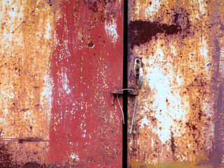 Old locked rusty door. The old iron background is painted in red, pink, purple with rust and chips.