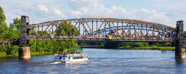 Tourist boat cruises under old historic iron bridge on Elbe River in Magdeburg, Germany with blue...