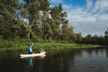 A woman floats on a SUP board on a river, smiles happily and waves at the camera, a man rafts on calm water alone, greeting with his hand, paddleboarding in equipment.