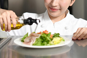 オリーブオイルをサラダにかける女性料理人