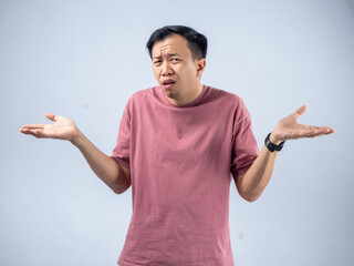 An Asian man in a pink shirt shrugs with a confused and uncertain expression, his arms outstretched...