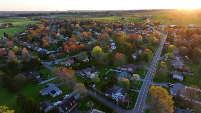 Magnificent suburb residential area with homes and buildings during sunset time. Colorful trees in rural area. Main Street in small town. Aerial forward wide shot.