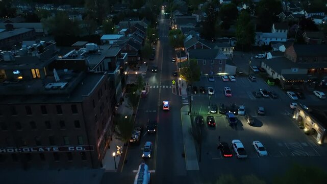 Police Car on main street in american town at night. Aerial tilt up wide shot. Establishing drone scene.