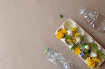 Egg carton, plastic bottle, fruit wrap and flowers on brown paper flat lay