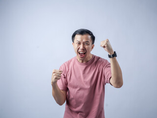 A man in a pink shirt raises both fists in a celebratory gesture, his face beaming with excitement...