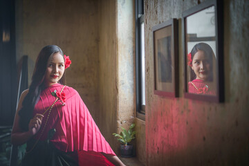 Beautiful portrait of an Asian female. A pretty woman wearing a red sash and green loincloth a traditional Thai dress costume. Asian tourists dress to blend in ancient Thai culture.
