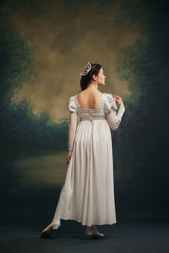 Timeless Grace. Elegant young woman in white dress with silver hair accessory standing against vintage green background. Juliette. Concept of history, comparison of eras, remake, beauty and fashion