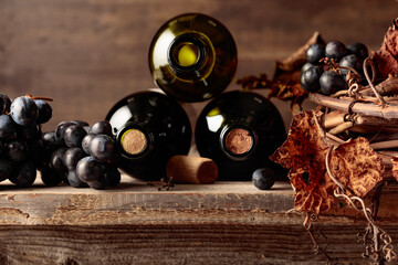 Bottles of red wine with grapes and dried vine on an old wooden table.