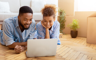 Obraz premium Moving Concept. Black Spouses Using Laptop Watching Movie Lying On Floor In New Apartment. Selective Focus, Free Space
