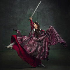 Powerful female warrior. Young emotional woman, royal person in dynamic pose with sword, showing determination and power against vintage green background. History, comparison of eras, remake concept