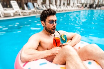 Handsome bearded guy drinking two cocktails while spending his holiday in the swimming pool. Summertime, holidays, lifestyle concept