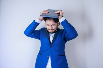 ノートパソコンを持ちながら頭を抱えるビジネスマン