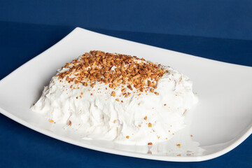 A mouthwatering sweet treat features a creamy, whipped topping generously sprinkled with crunchy almond pieces on a white plate against a deep blue background. Homemade dessert.