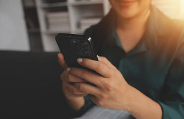 Charming young Asian woman using cellphone, communicating on web, working or learning online, sitting in armchair against white wall, free space. Lovely millennial lady chatting on smartphone
