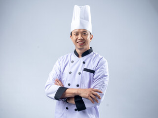 A confident Asian male chef in a white uniform and hat, standing with arms crossed and smiling, exudes professionalism and expertise against a light blue background