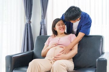 An Asian young husband gently embraces his pregnant wife at home, their love evident as they prepare for parenthood, cherishing the tender moments of expecting their first child together.