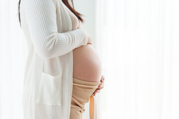 An Asian young pregnant wife relaxes at home, her hand gently resting on her belly, filled with love and anticipation as she embraces the journey of impending motherhood.