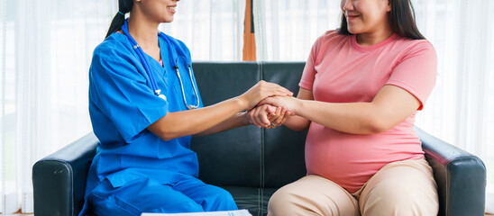 Asian female doctor and nurse consult with a pregnant woman on a sofa, using an ultrasound and stethoscope, preparing her for birth ahead of schedule with care and expertise.