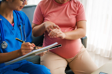 Asian female doctor nurse encouragement to a pregnant woman on a sofa, using ultrasound and stethoscope, addressing medical conditions like edema, varicose veins, and pregnancy-induced hypertension.