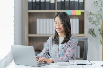 Sharing good business news. Attractive young businesswoman talking on the mobile phone and smiling while sitting at her working place in office and looking at laptop PC.