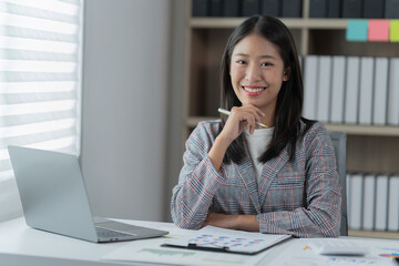 Sharing good business news. Attractive young businesswoman talking on the mobile phone and smiling while sitting at her working place in office and looking at laptop PC.