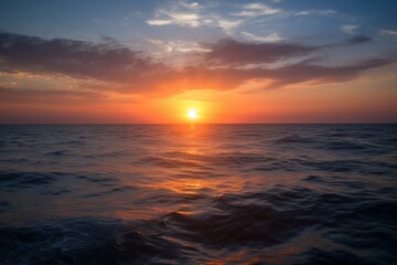 Fototapeta premium A breathtaking sunset over the ocean, with the sun setting on the horizon and casting a warm, golden glow over the water. The sky is painted with vibrant hues of orange, red, and blue