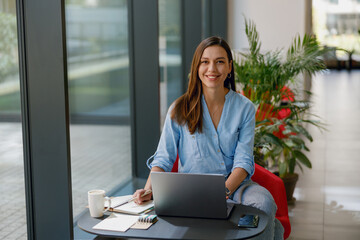 Confident woman working remotely on a laptop in a modern office with greenery and technology