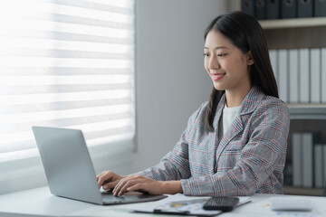 Sharing good business news. Attractive young businesswoman talking on the mobile phone and smiling while sitting at her working place in office and looking at laptop PC.