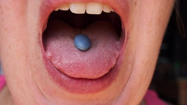 A woman puts a blue pill on her tongue. Close-up of her taking the tablet.  