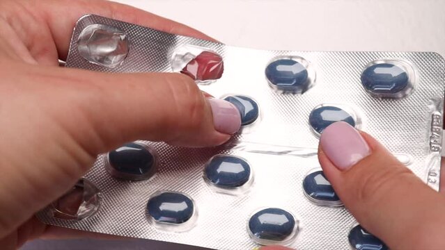 A girl squeezes a blue capsule from a silver blister pack containing blue pharmaceutical capsules. The concept of medication and vitamins.