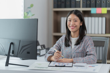 Sharing good business news. Attractive young businesswoman talking on the mobile phone and smiling while sitting at her working place in office and looking at laptop PC.