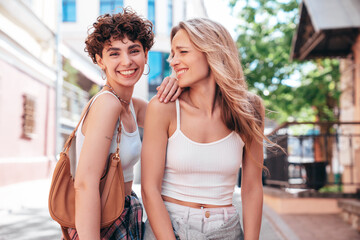 Two young beautiful smiling hipster female in trendy summer white t-shirt and shorts clothes. Sexy carefree women posing in the street. Positive models having fun, hugging and going crazy