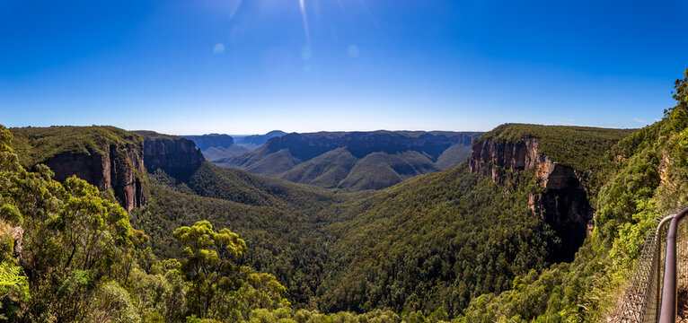 Govetts Leap Lookout, a panoramic view of the Blue Mountains National Park in New South Wales, Australia, featuring a lush valley, rugged cliffs, and a clear blue sky.