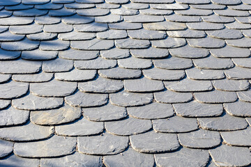 Close-up view of overlapping grey slate roof tiles aligned in an orderly and uniform pattern, showcasing the material’s texture and traditional architectural style.