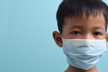 Close up Asian Boy wearing health mask isolated on blue background. Medical and health concept. Human population viruses, infections, flu disease prevention